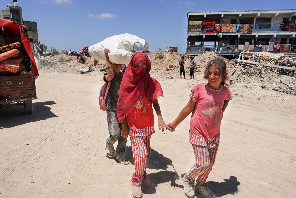 Two children walk hand in hand down a dirt road.