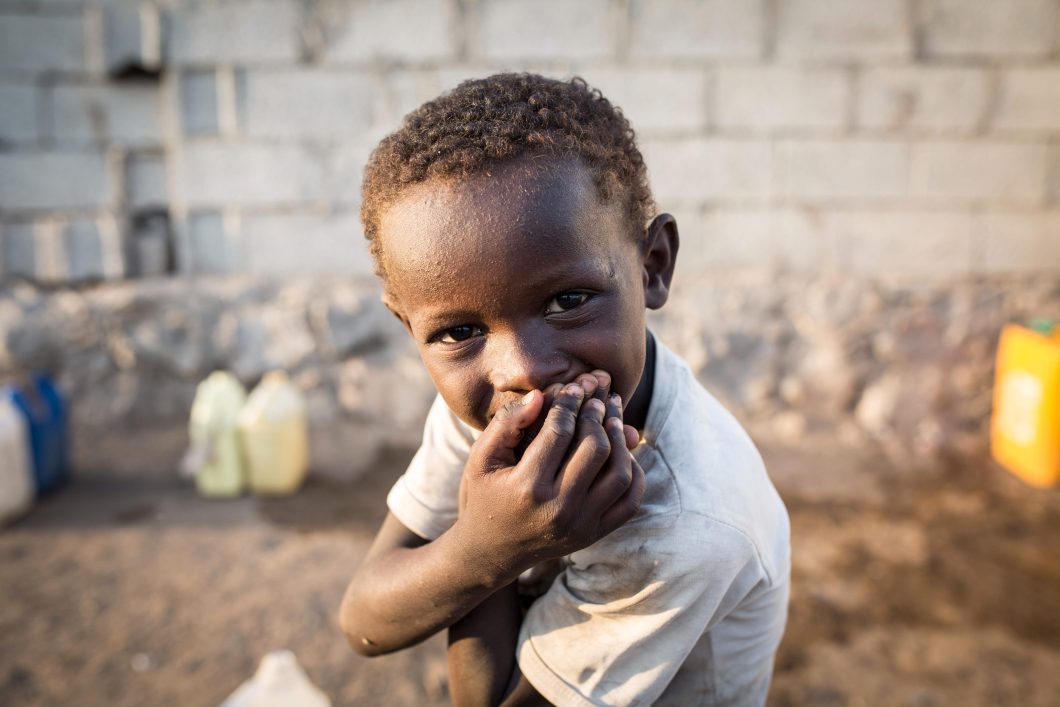 Young boy sitting in front of water bottles lining a wall with hands on face.