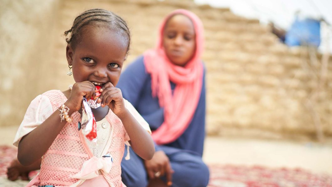 Achta from Chad eats ready-to-use therapeutic food, while her mother looks on behind her.