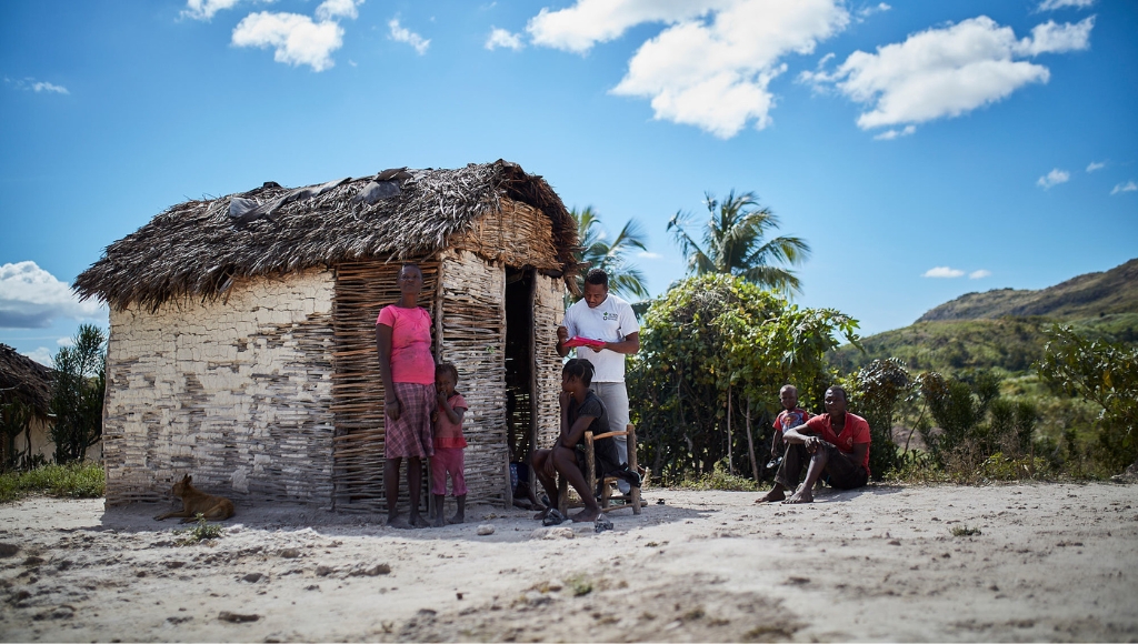 Family in Haiti stand outside their home in sunny, tropical surroundings.