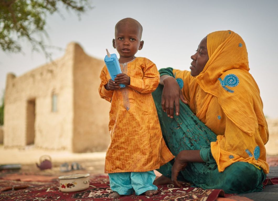 Moustafa in his mother from Chad in colourful yellow and green clothes standing on patterned rug.