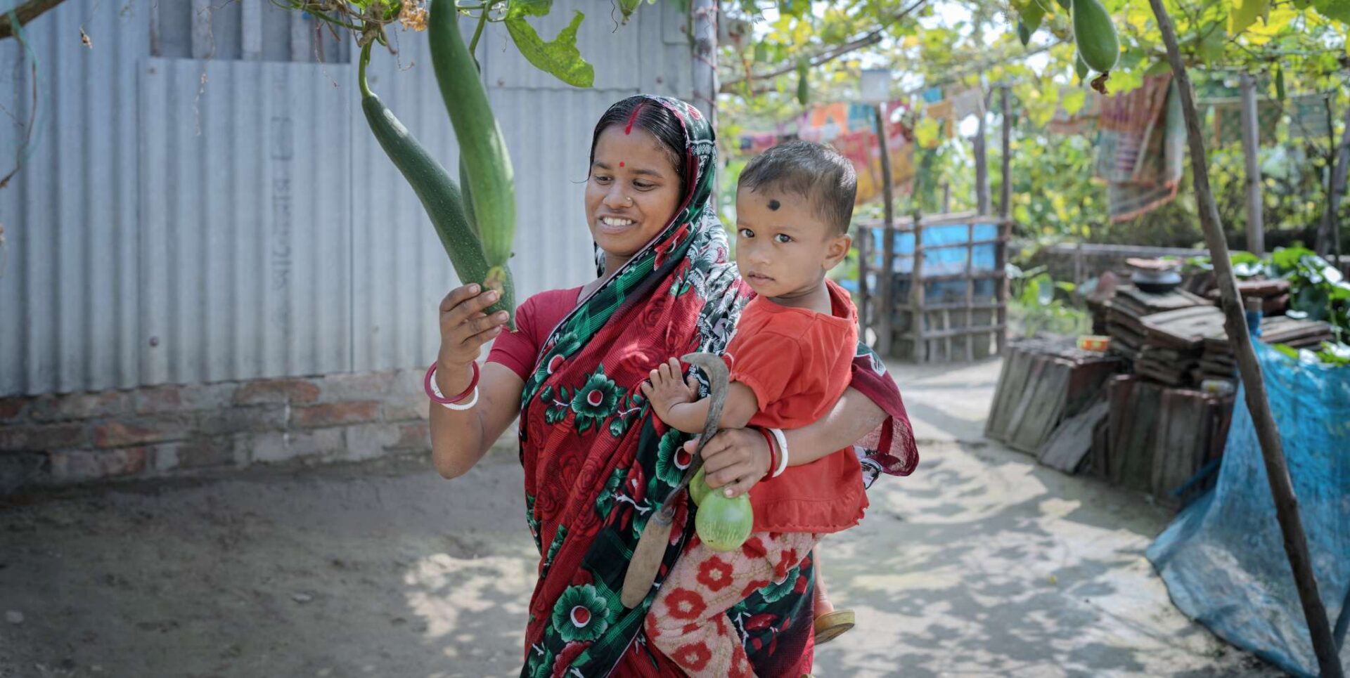 Kobita from Bangladesh examines her crops while holding her child.