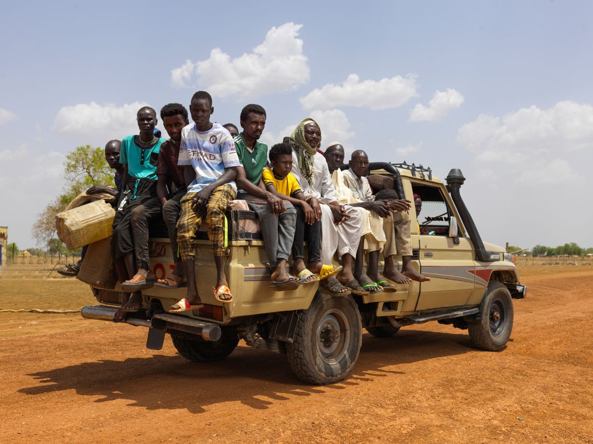 South Sudanese families sit on truck in desert surroundings.